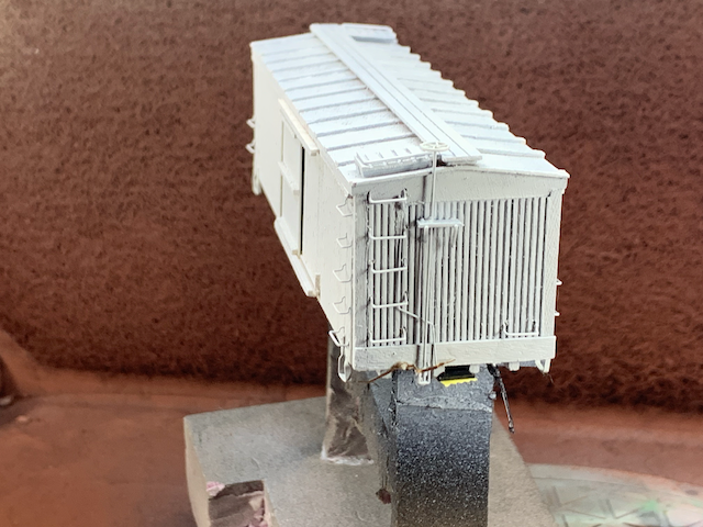 HO scale box car in paint booth with a layer of gray primer, B end view.