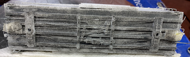 HO scale box car in paint booth with a layer of gray primer, underside view.