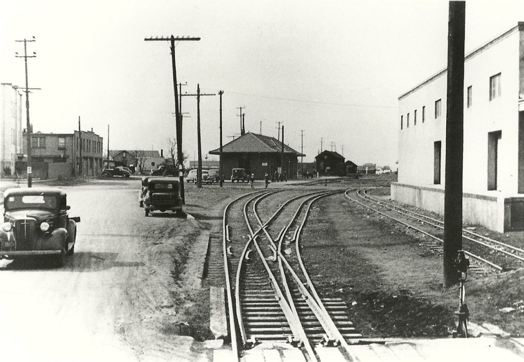 Black & white photo of Santa Fe in the 1930s with a road on the left and dual gauge track on the right.