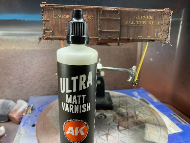 Heavily weathered HO scale UP box car, post-oil weathering, in the spray booth behind a bottle of AK Ultra Matt Varnish.