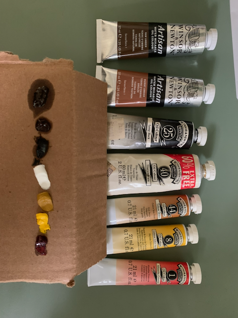 A collection of earth-toned oil paints that has been let out onto cardboard to soak up excess linseed oil.
