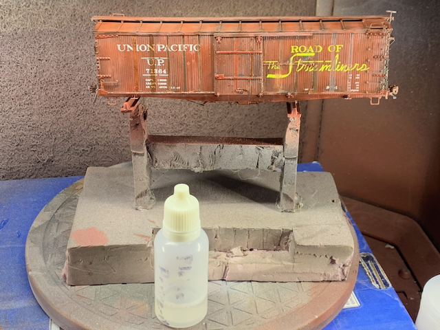 Heavily weathered HO scale UP box car in the paint booth next to a bottle of Pledge being used as a semi-gloss coat.