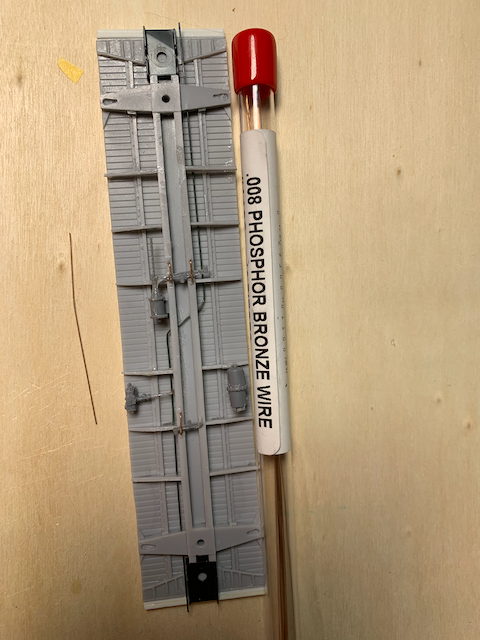 HO scale box car floor with brake detail being installed. A package of 0.008 phosphor bronze wire is present.