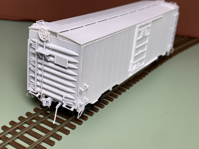 HO scale box car, primed in white, on dual gauge track.
