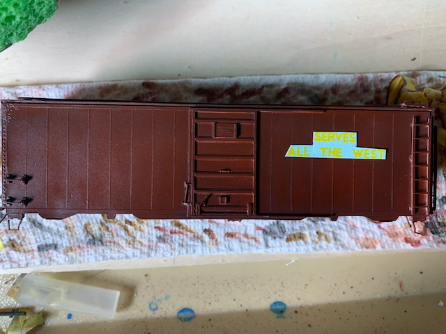 Freshly painted box car with the decal logo reading "SERVES ALL THE WEST" cut out and in place but not applied yet.